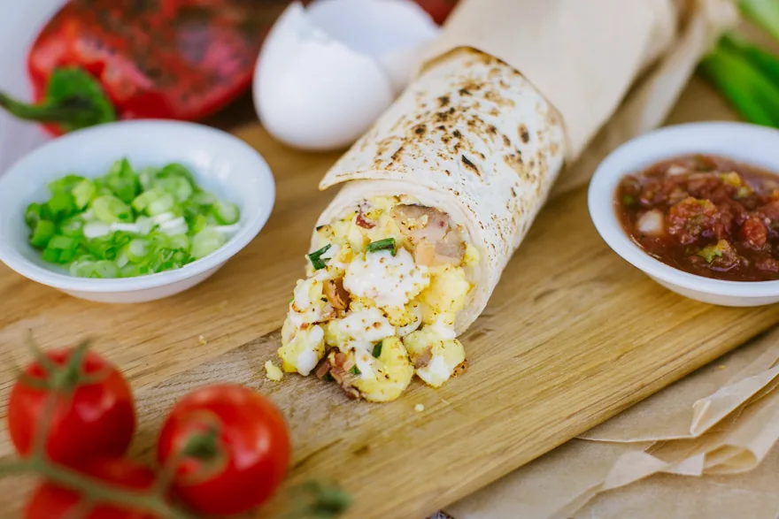 Breakfast burrito cut open on a board beside salsa and scallions