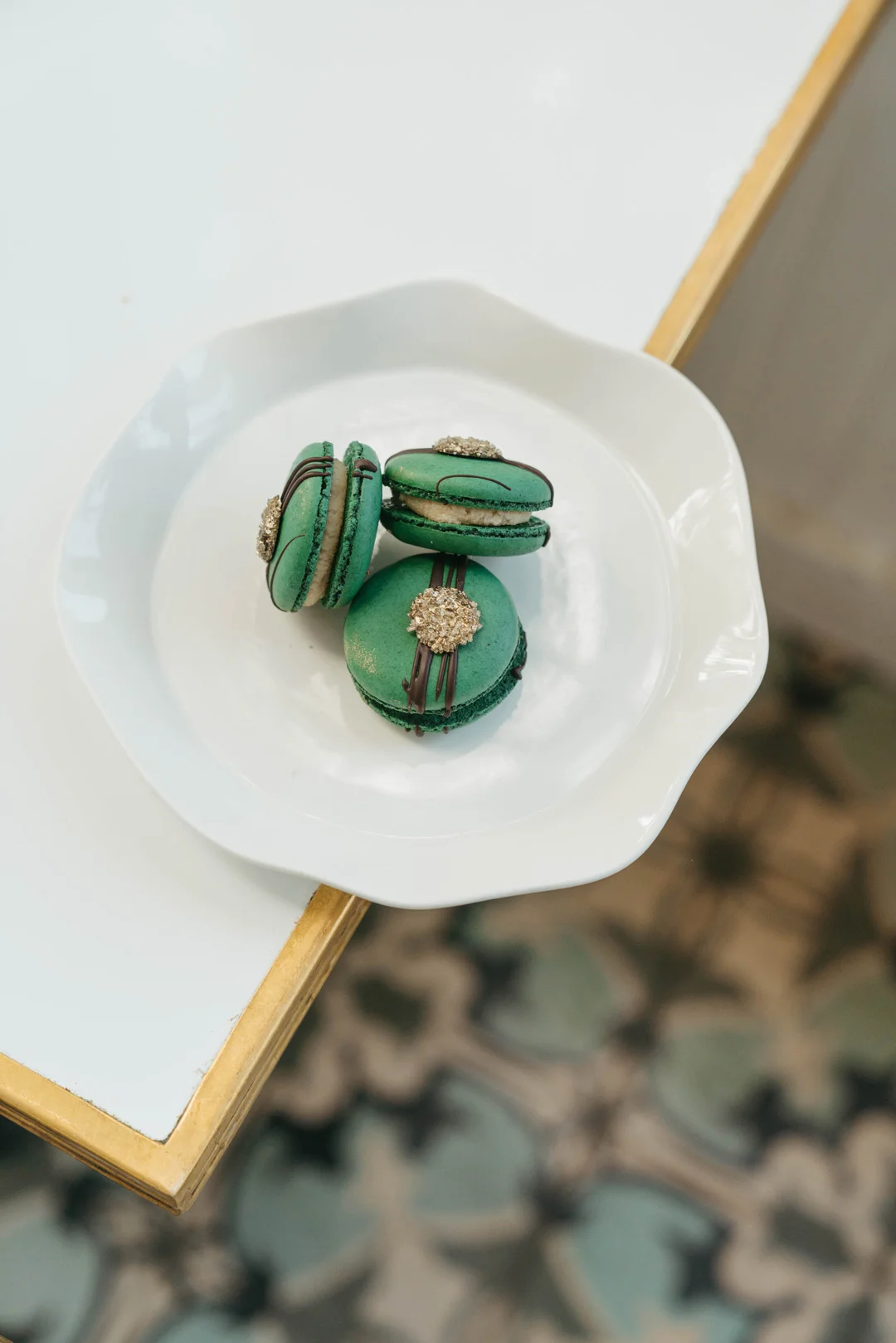 Three green macarons with chocolate drizzle and gold sprinkles