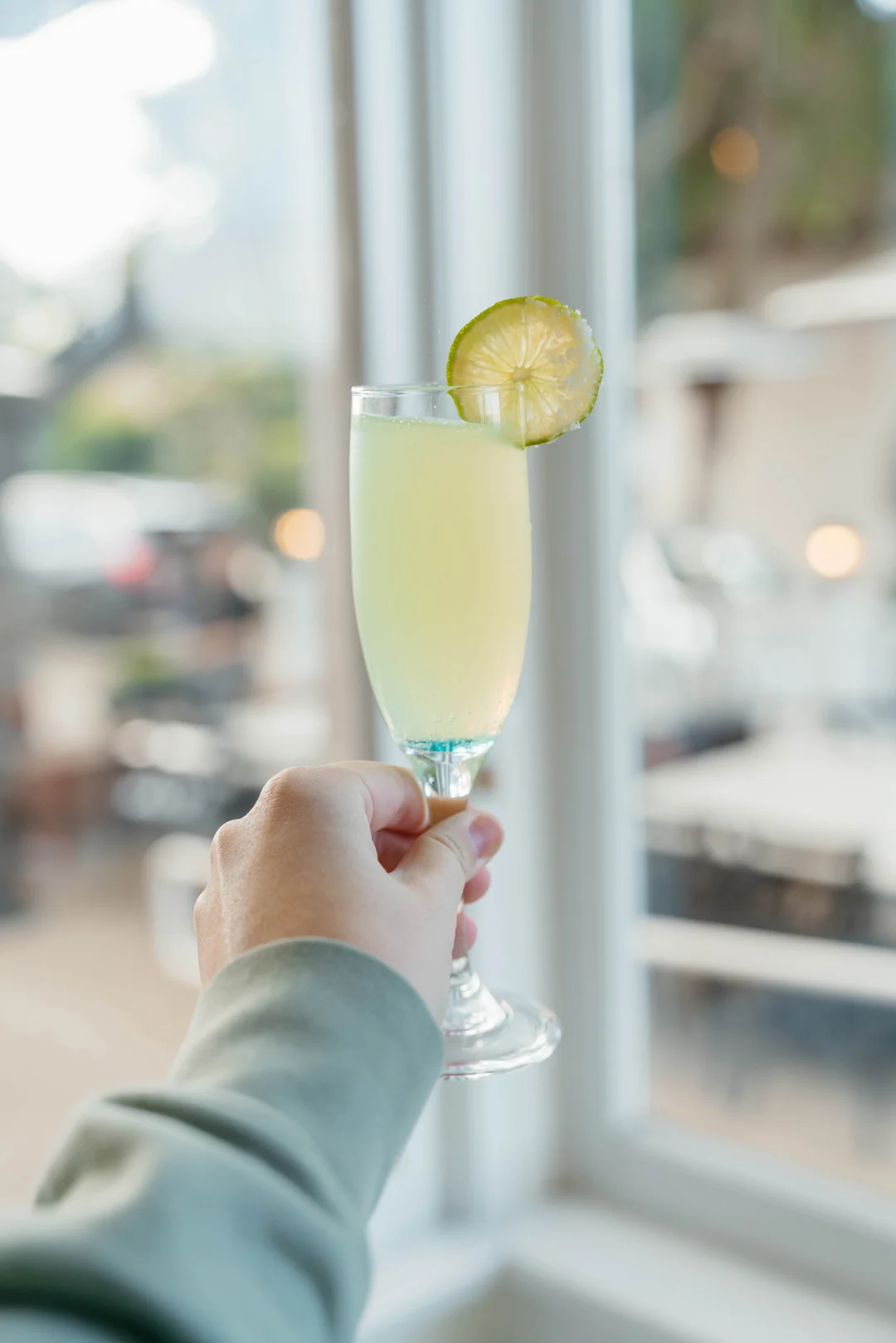 Hand holding a pale green mimosa with a lime wheel