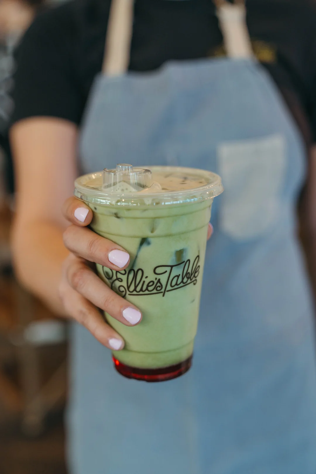 Hand holding iced matcha over red strawberry syrup