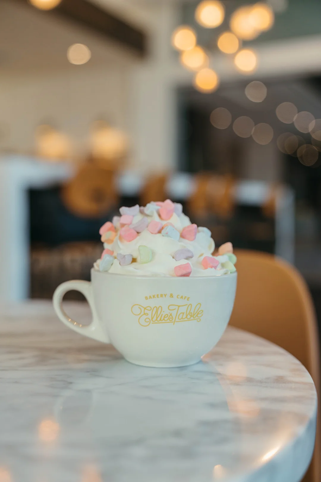 Hot drink topped with whipped cream and pastel marshmallows in an Ellie’s Table mug