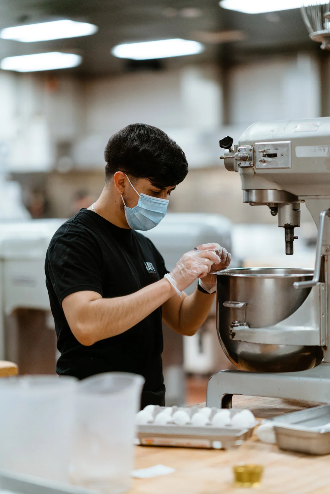 Masked kitchen employee working beside a stand mixer