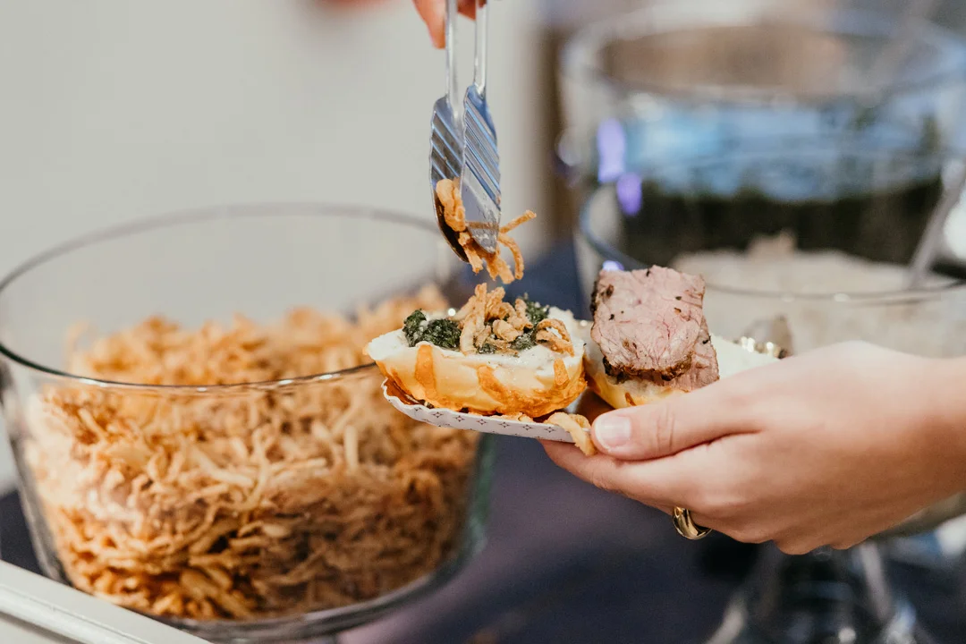 Hand adding fried onions to an open roast beef slider