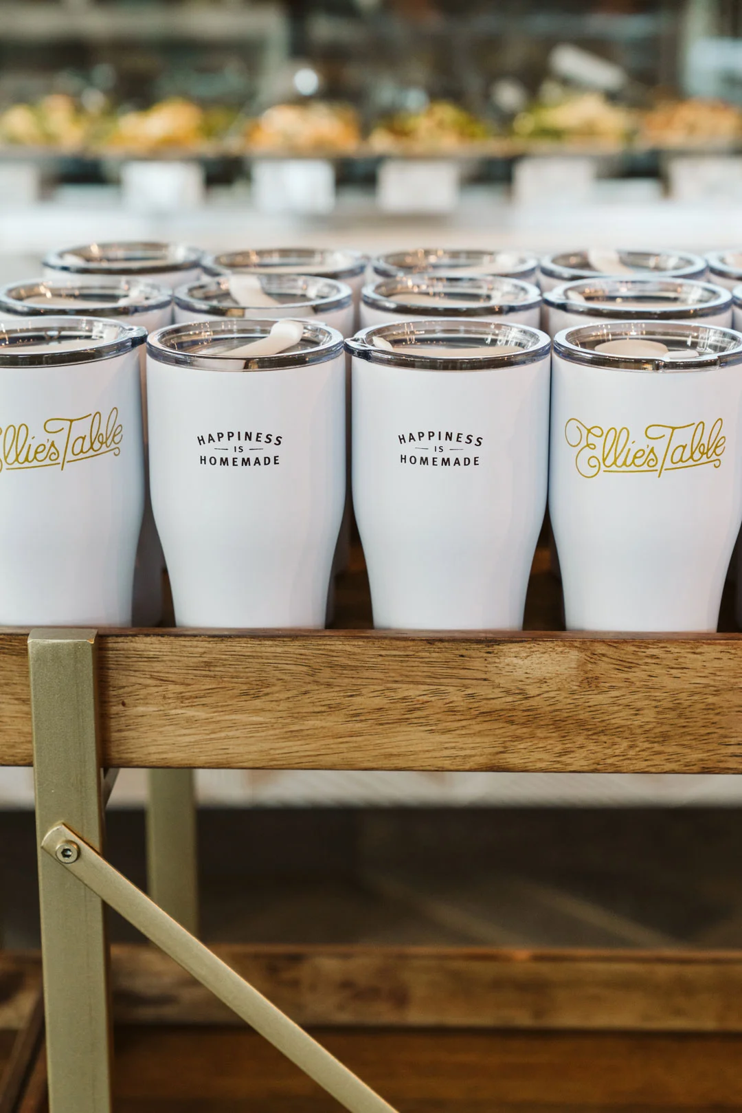 Rows of Ellie's Table travel mugs displayed on a wooden shelf