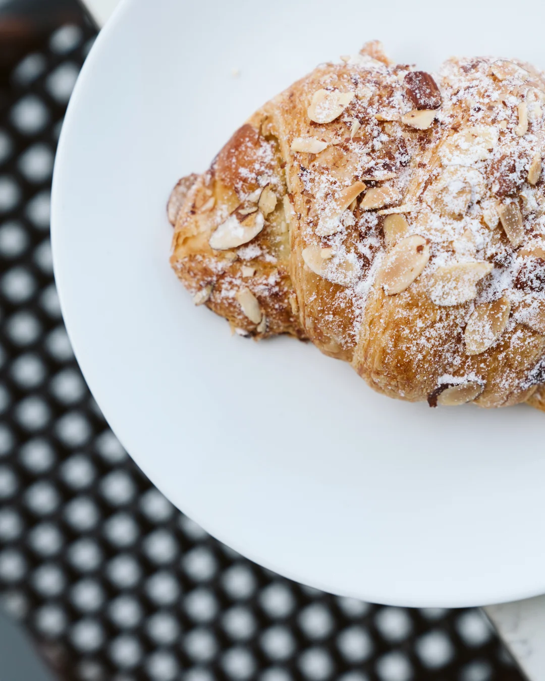 Almond croissant dusted with powdered sugar on a white plate