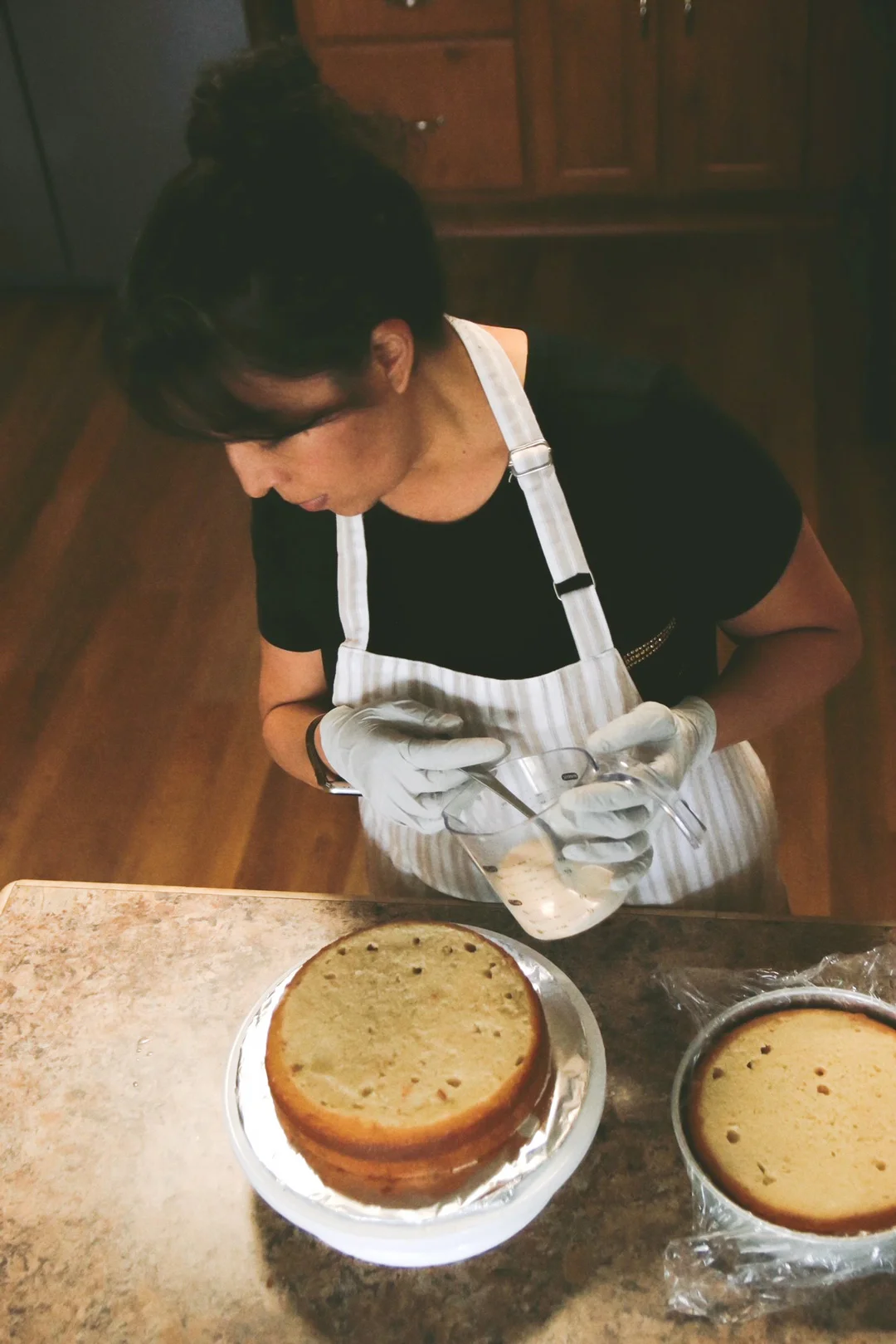 Claudia pouring milk over two round tres leches cake layers