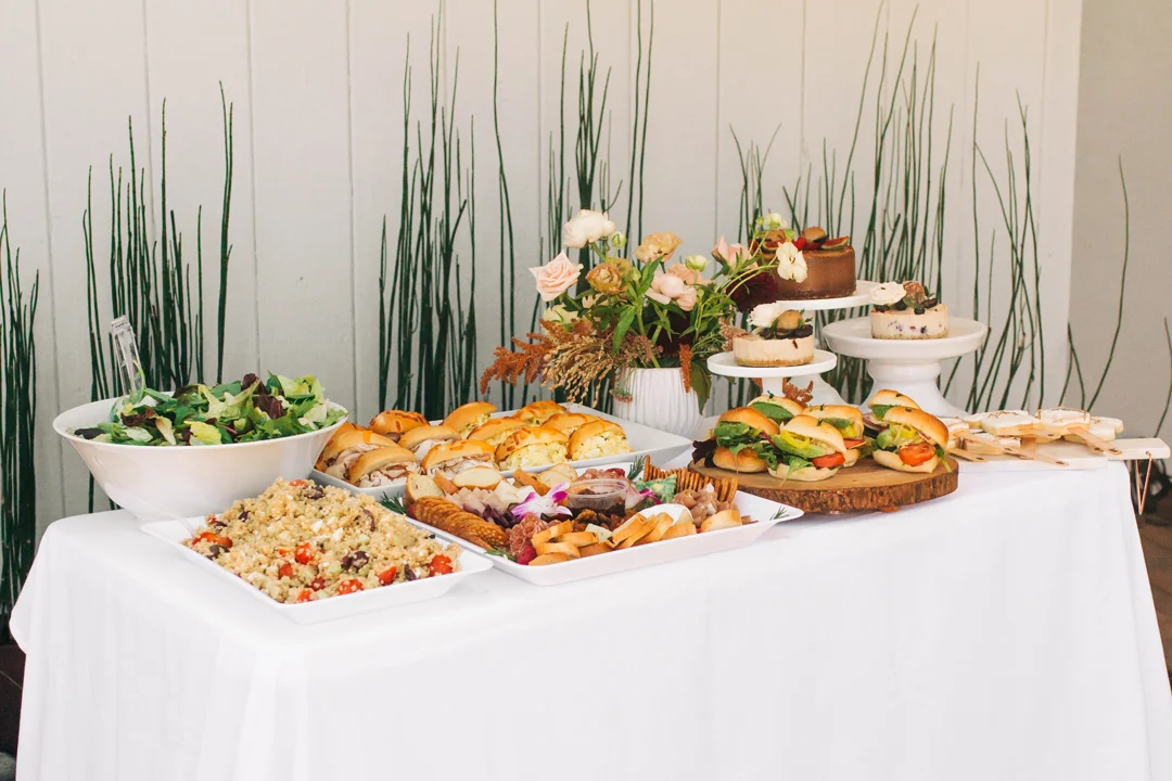 Baby shower grazing table with salads, sandwiches, pastries, and flowers
