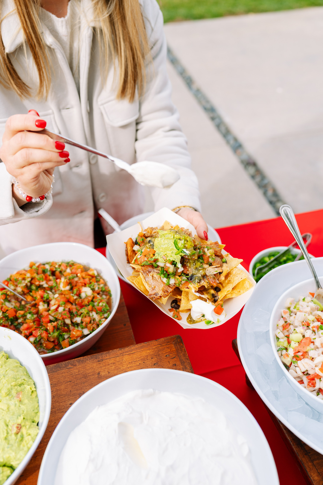 Girl scoops sour cream on top of her loaded nachos for a Super Bowl Sunday appetizer.