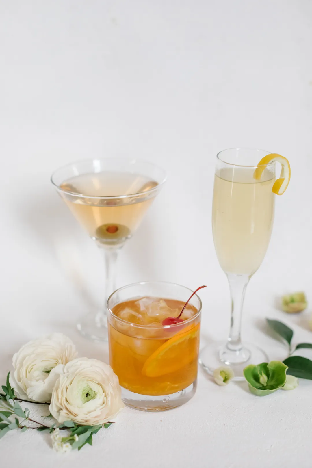 Martini, citrus cocktail, and sparkling drink beside white flowers