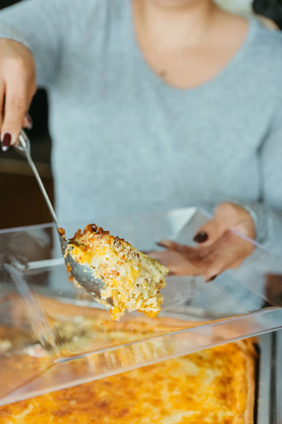 Person serving a baked casserole from a buffet pan
