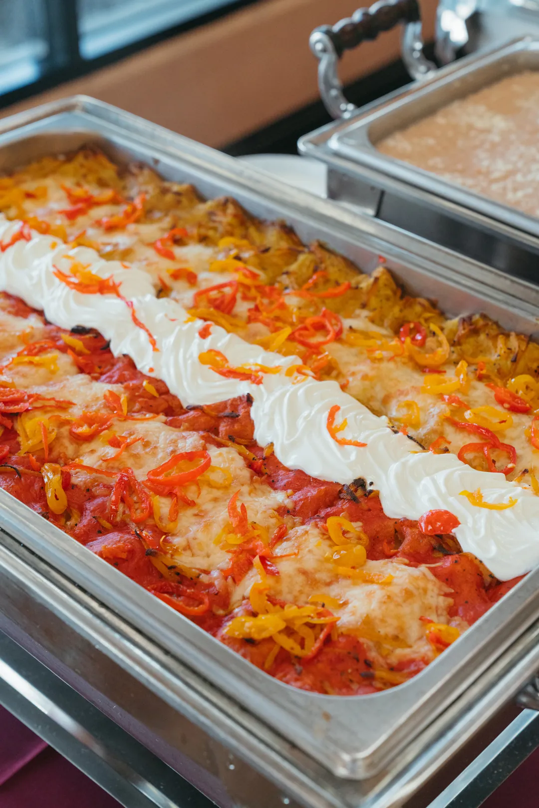 Red and green enchiladas with cheese, peppers, and a stripe of sour cream in a buffet pan