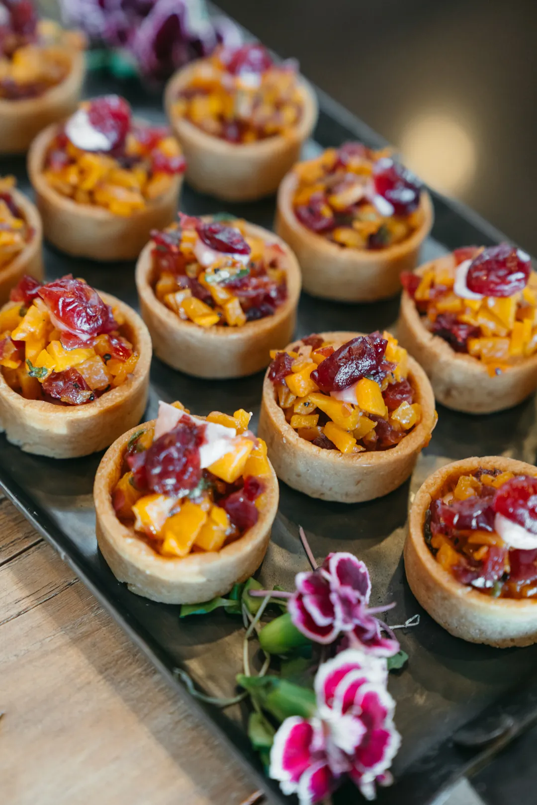 Tray of bite-size fruit tarts topped with berries and sliced fruit
