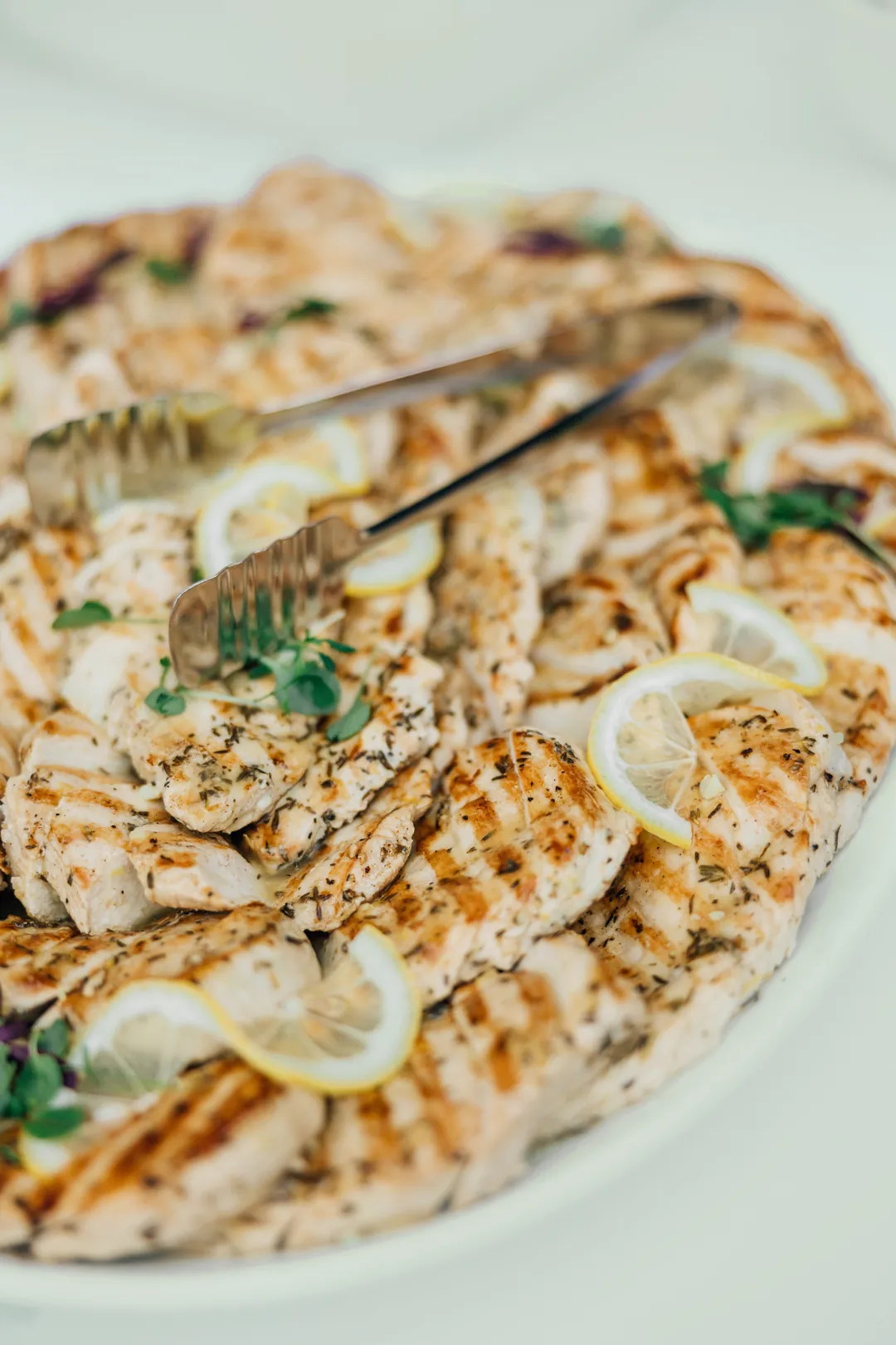 Sliced grilled chicken breasts garnished with lemon and herbs