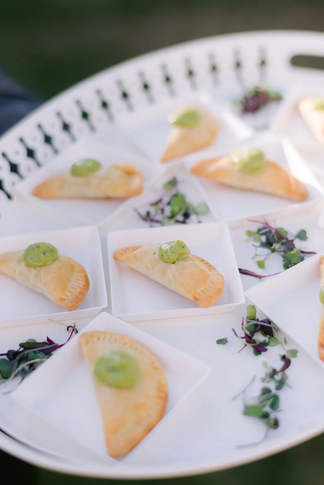 Mini empanadas topped with green sauce and served with microgreens