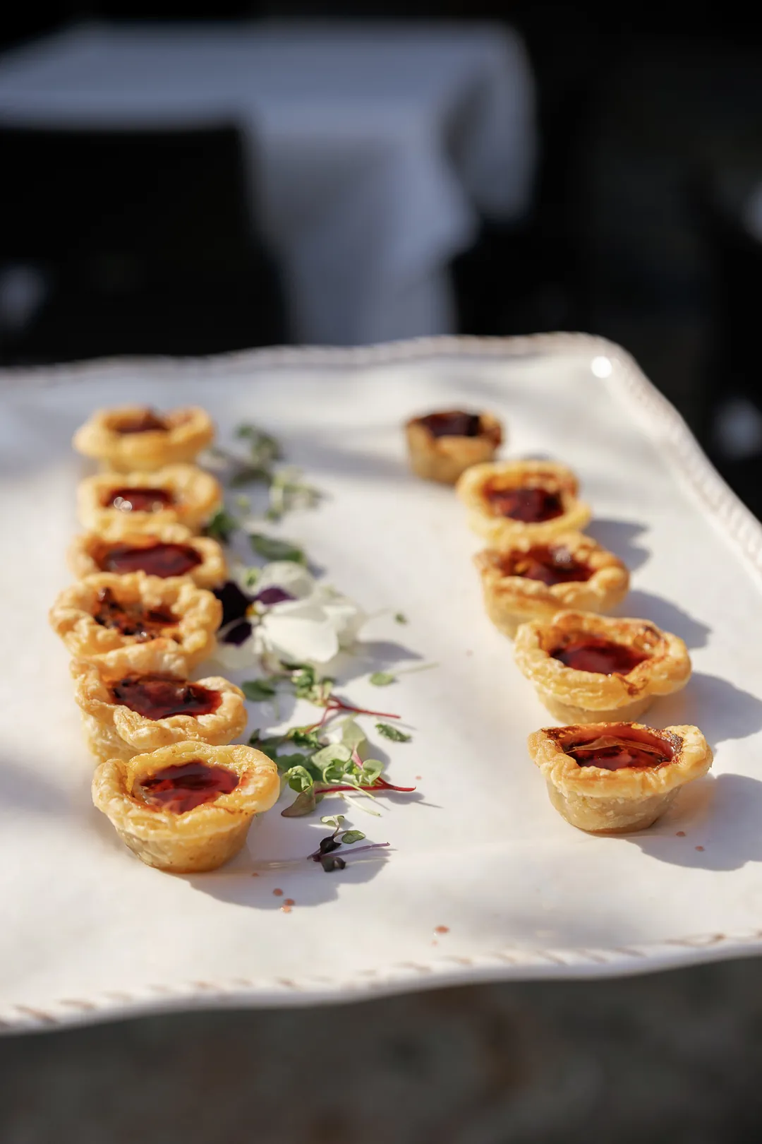 Rows of small jam tartlets on a white serving platter