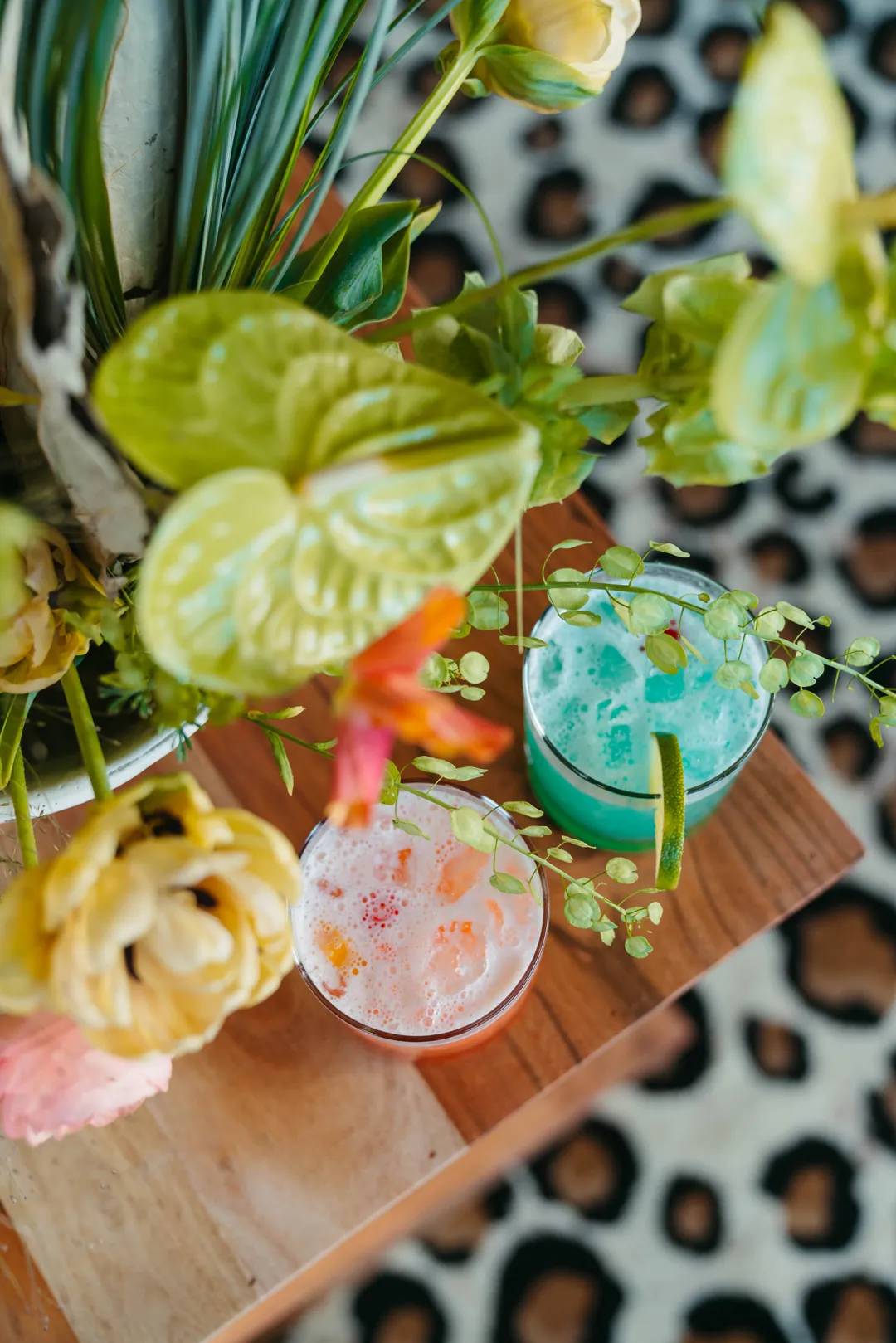 Two colorful cocktails beside a tropical floral arrangement