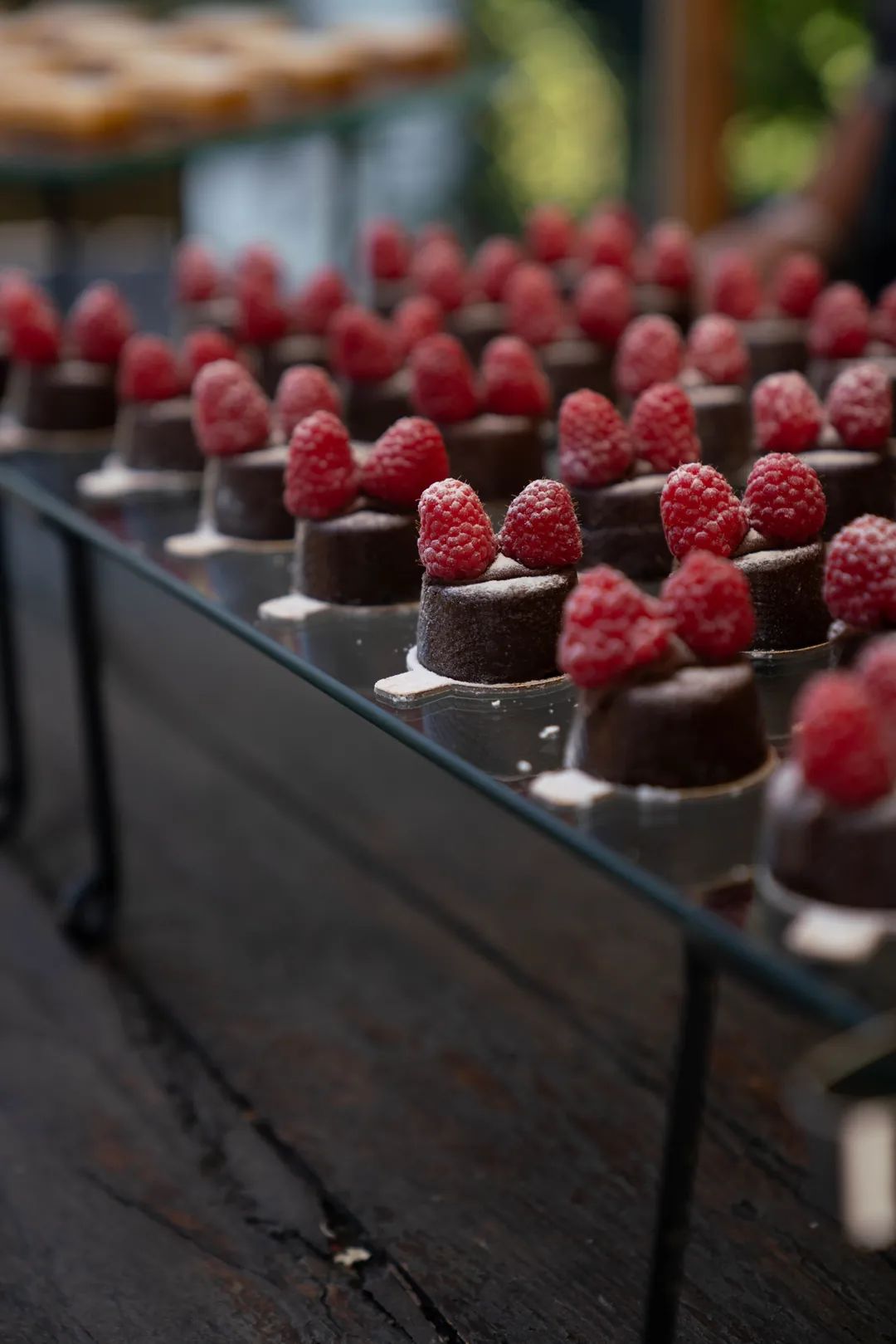 Rows of small chocolate cakes topped with raspberries