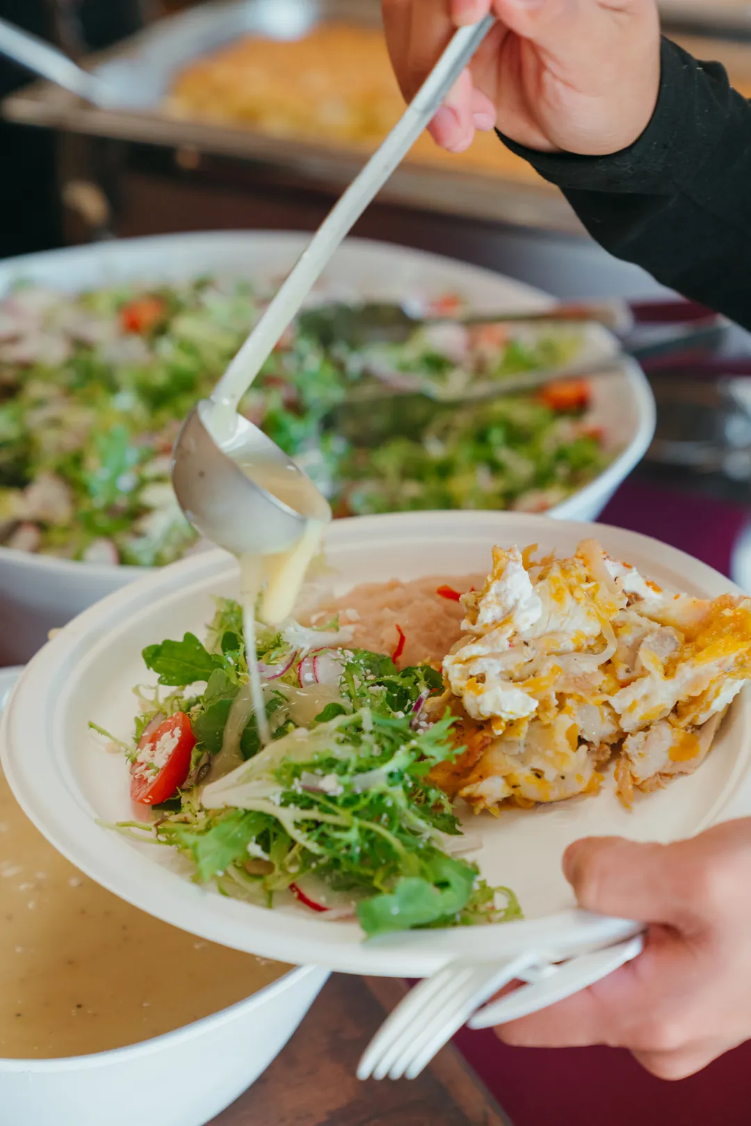 Guest spooning sauce onto a buffet plate with salad and an entrée