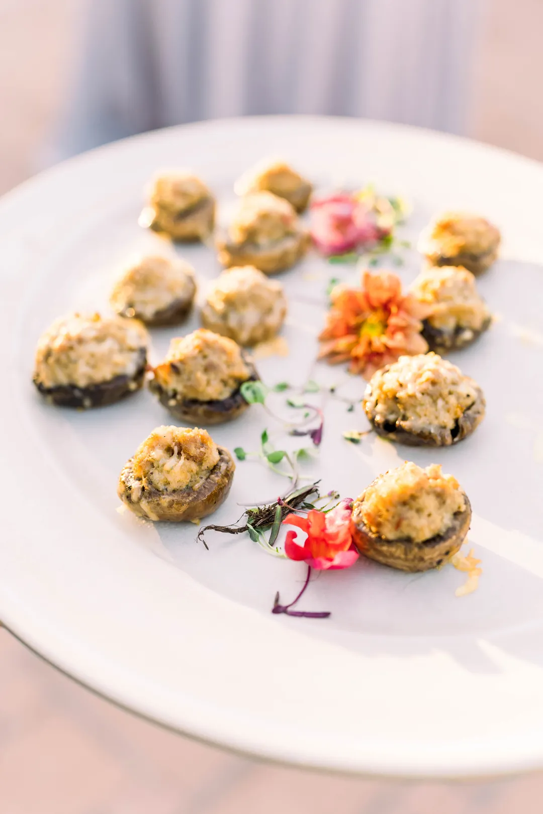 Stuffed mushrooms arranged around edible flowers on a white platter