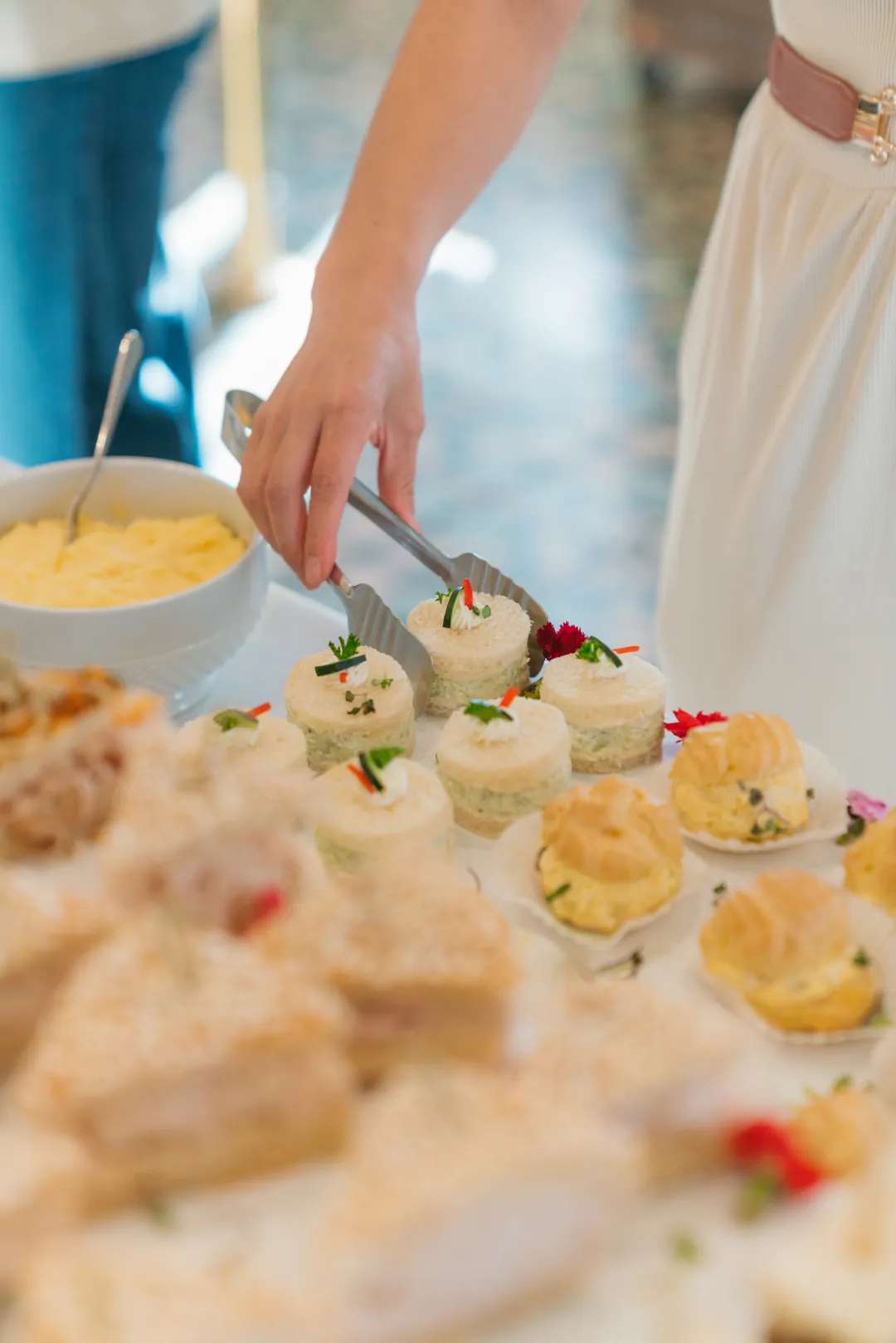 Guest using tongs to select a round cucumber tea sandwich
