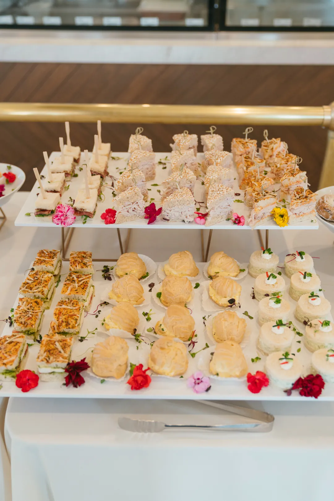Tiered trays of tea sandwiches and filled pastry puffs with white flowers
