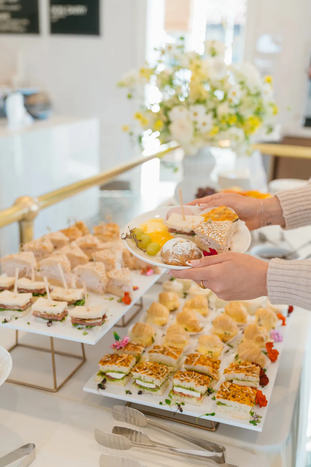Guest holding a plate of fruit, pastries and sandwiches at the tea buffet