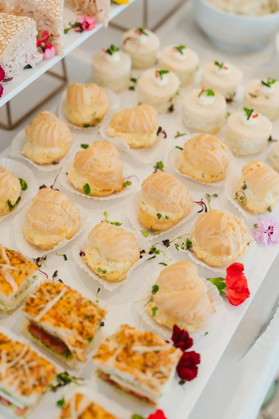 Filled savory pastry puffs beside tea sandwiches