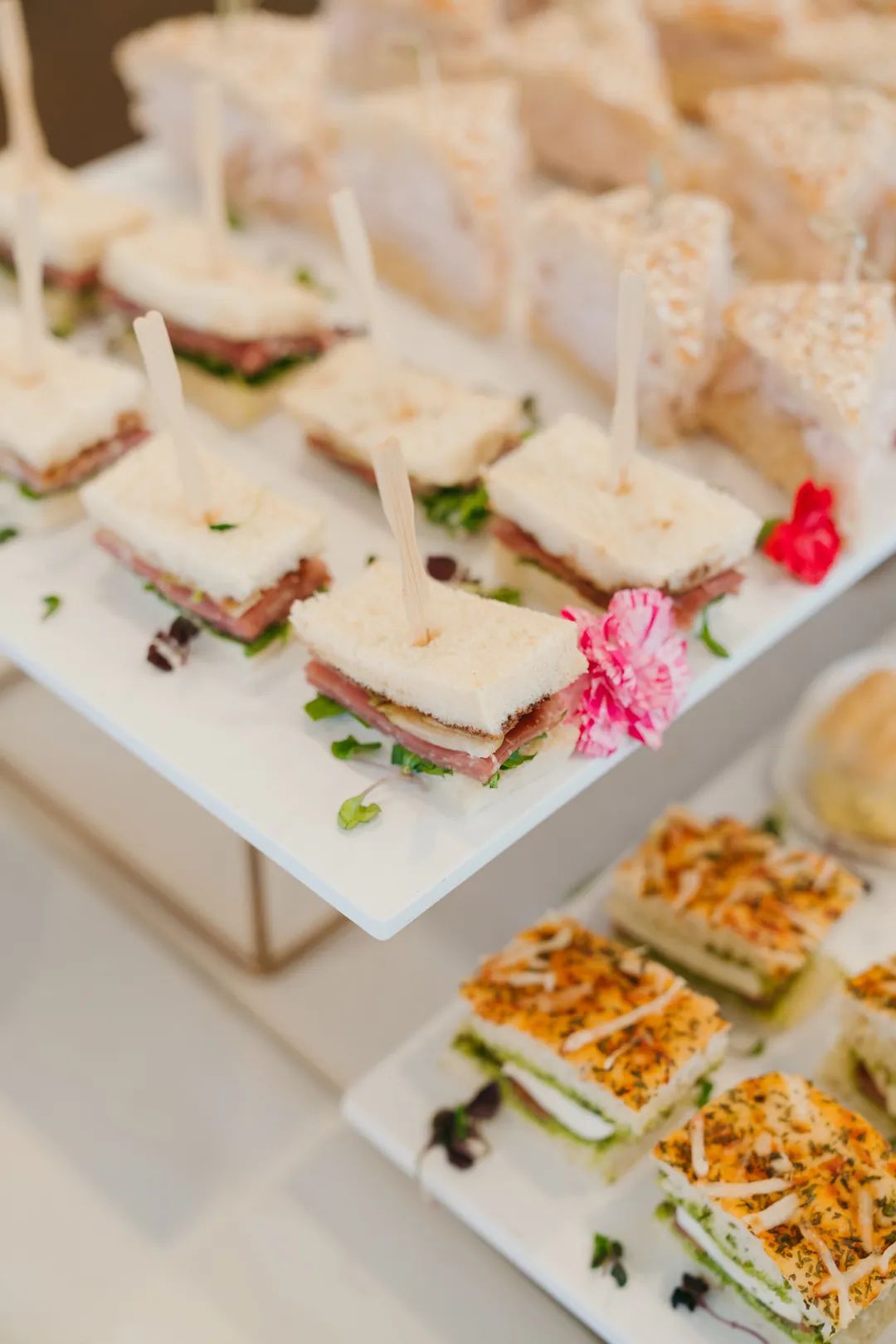 Finger sandwiches with sliced meat and greens beside focaccia sandwiches