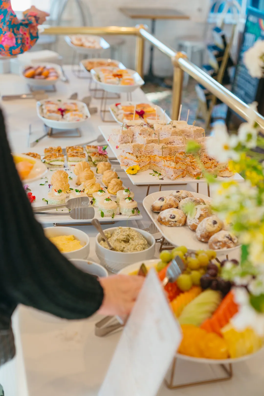 Guest selecting fruit from a tea buffet with sandwiches and pastries