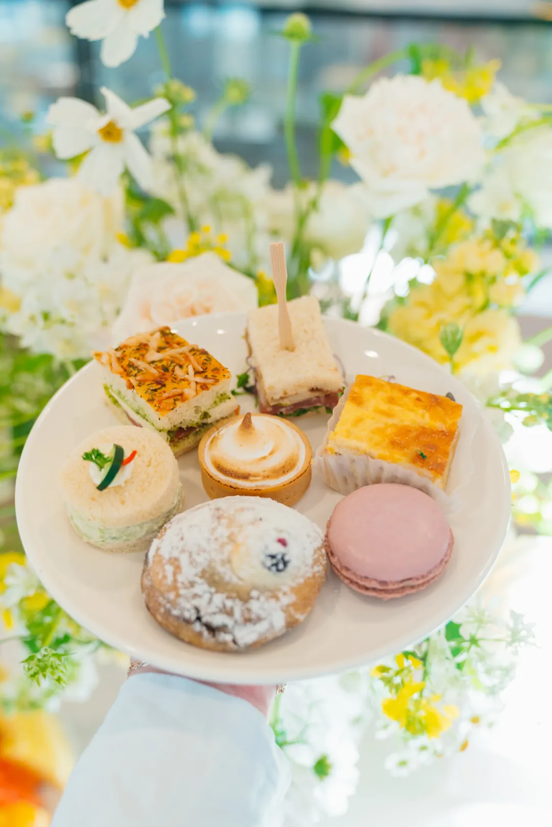 Plate with tea sandwiches, a lemon tart, quiche, berry pastry and pink macaron