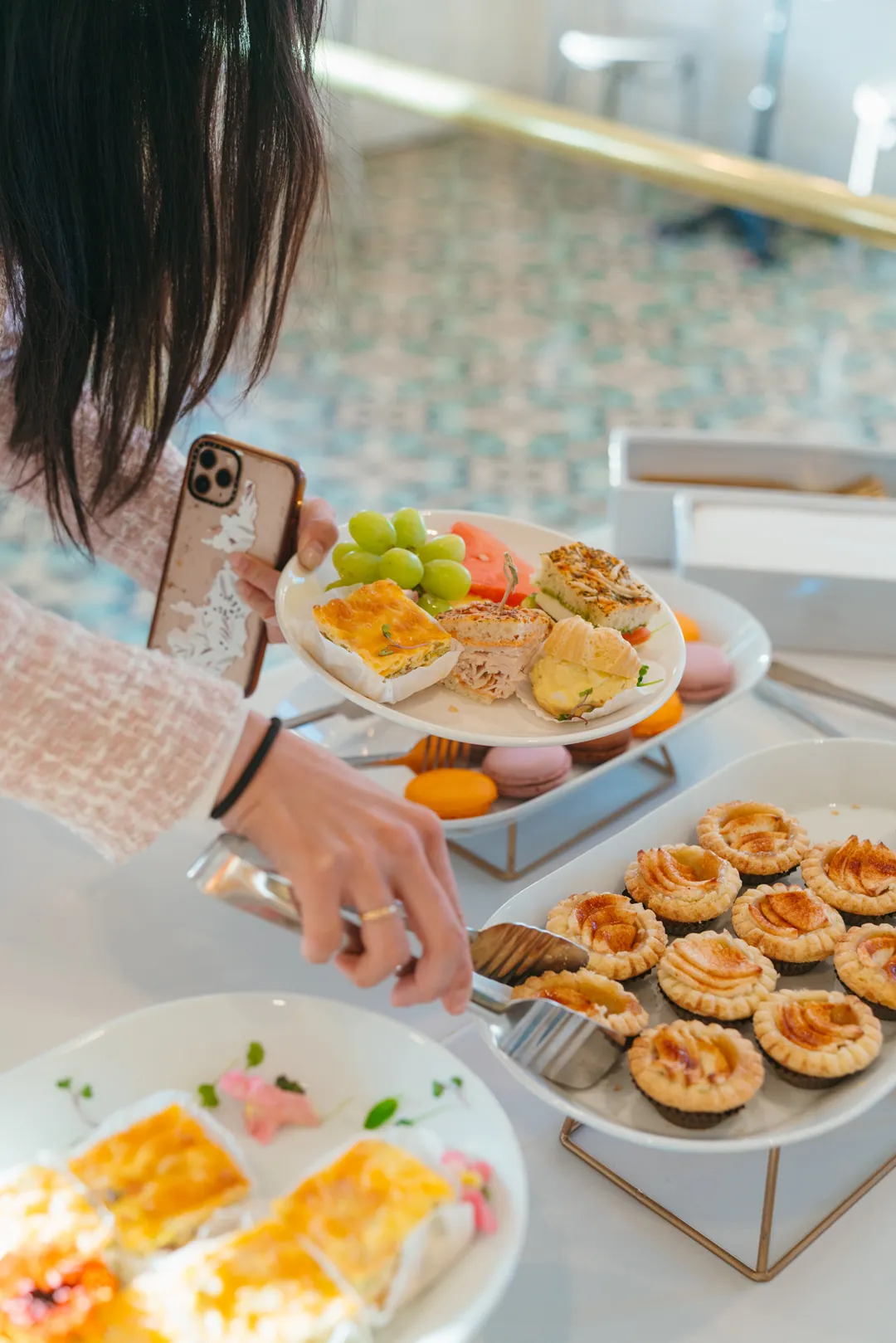 Guest holding fruit, sandwiches, quiche and a pastry while serving an apple tart