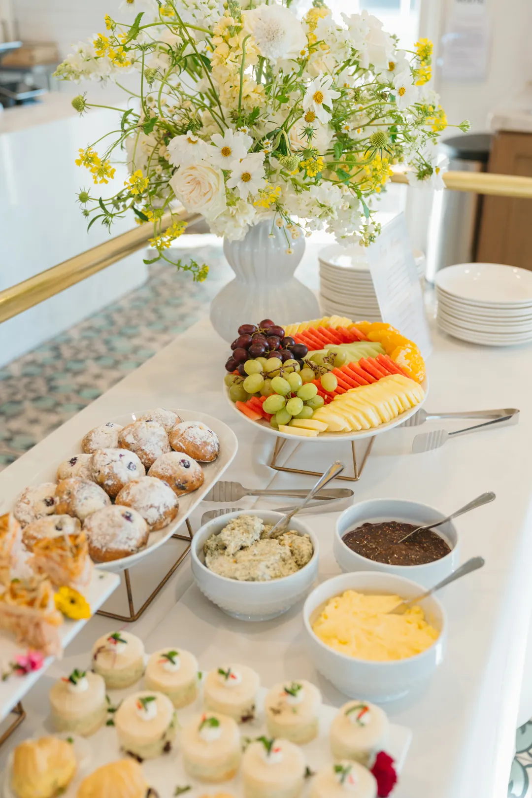 Fruit and powdered pastries beside spreads and white and yellow flowers