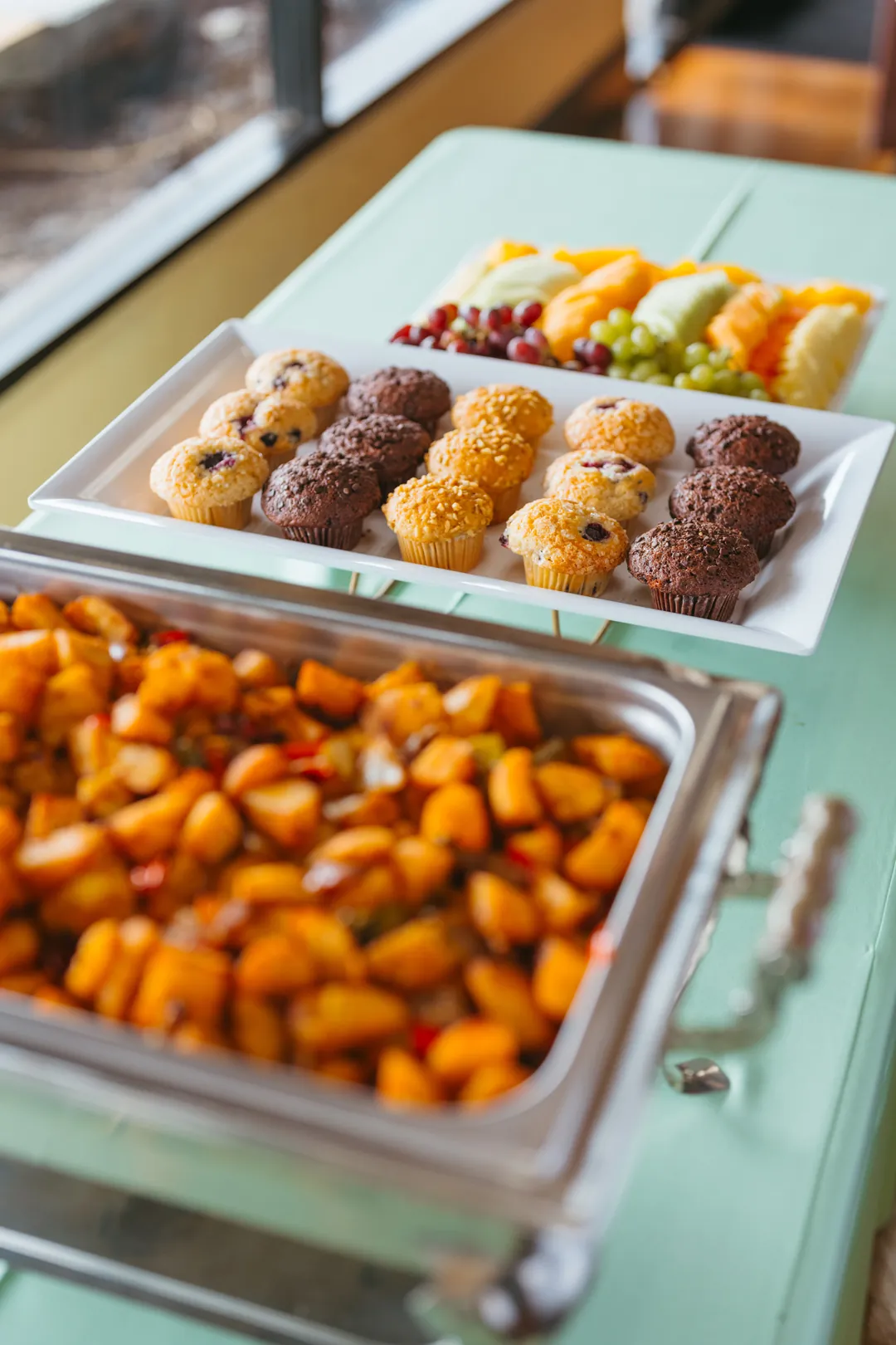 Trays of muffins, fruit and roasted breakfast potatoes
