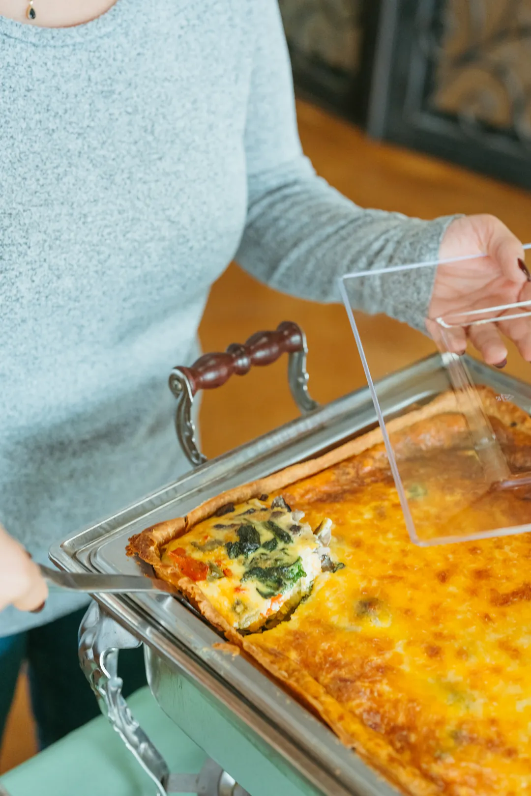 Guest lifting a vegetable deep-dish quiche slice with spinach and mushrooms
