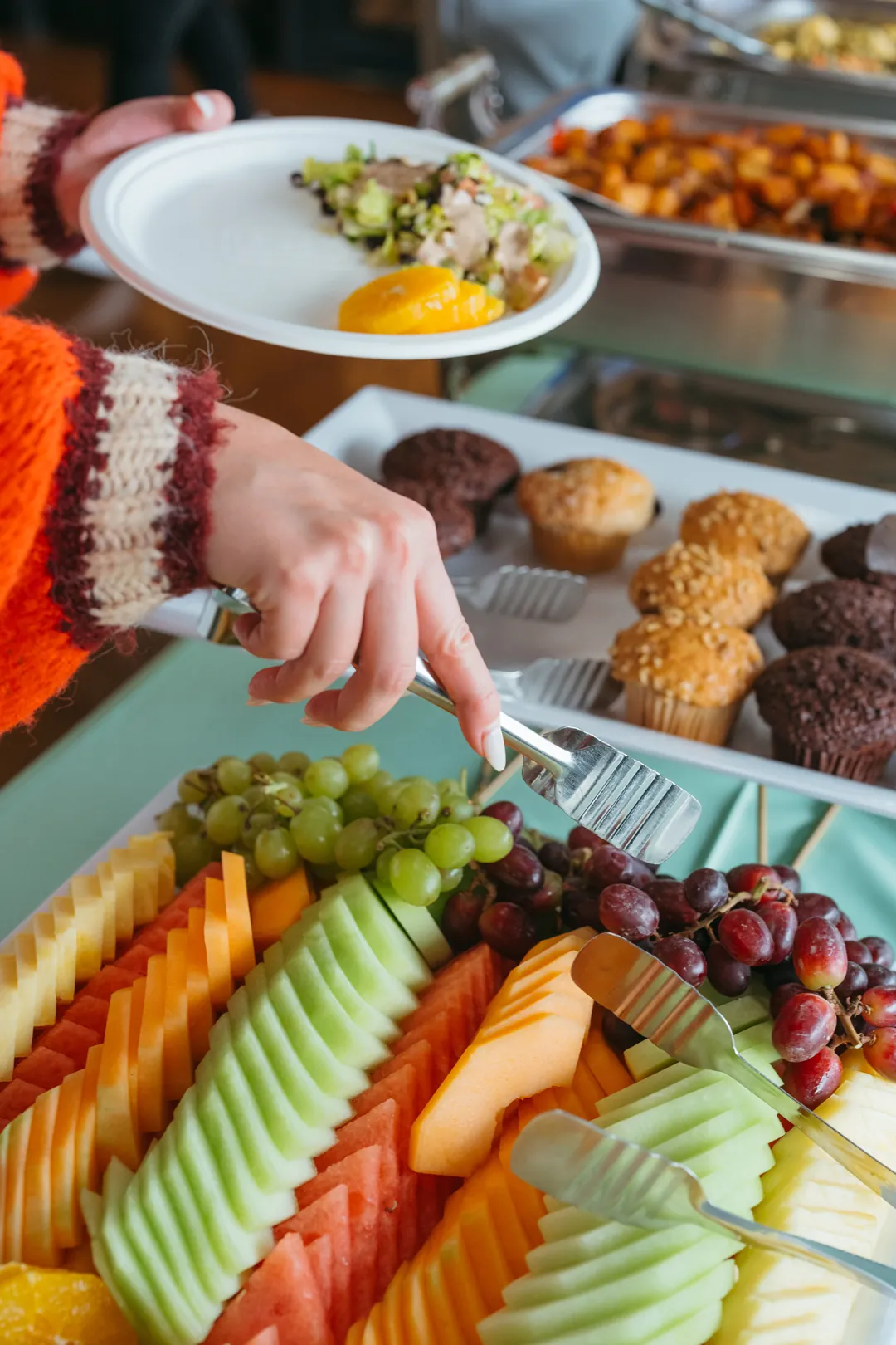 Guest serving fruit beside muffins and roasted potatoes