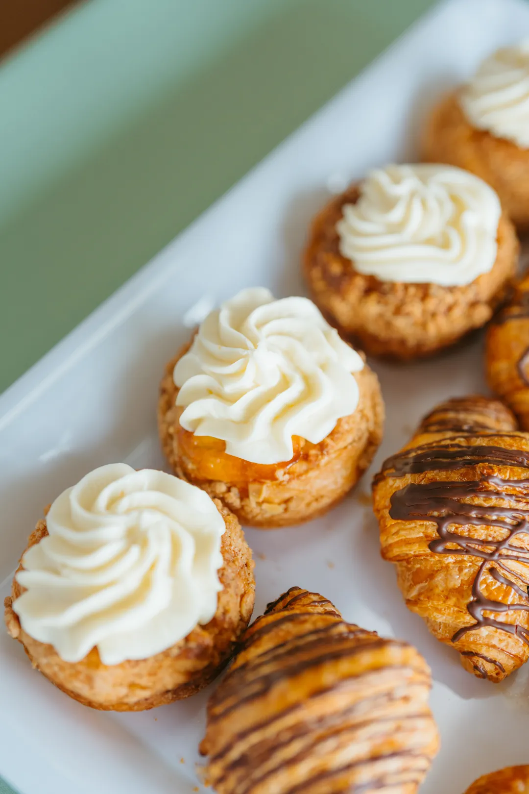 Cream-topped crumb pastries beside chocolate-drizzled croissants