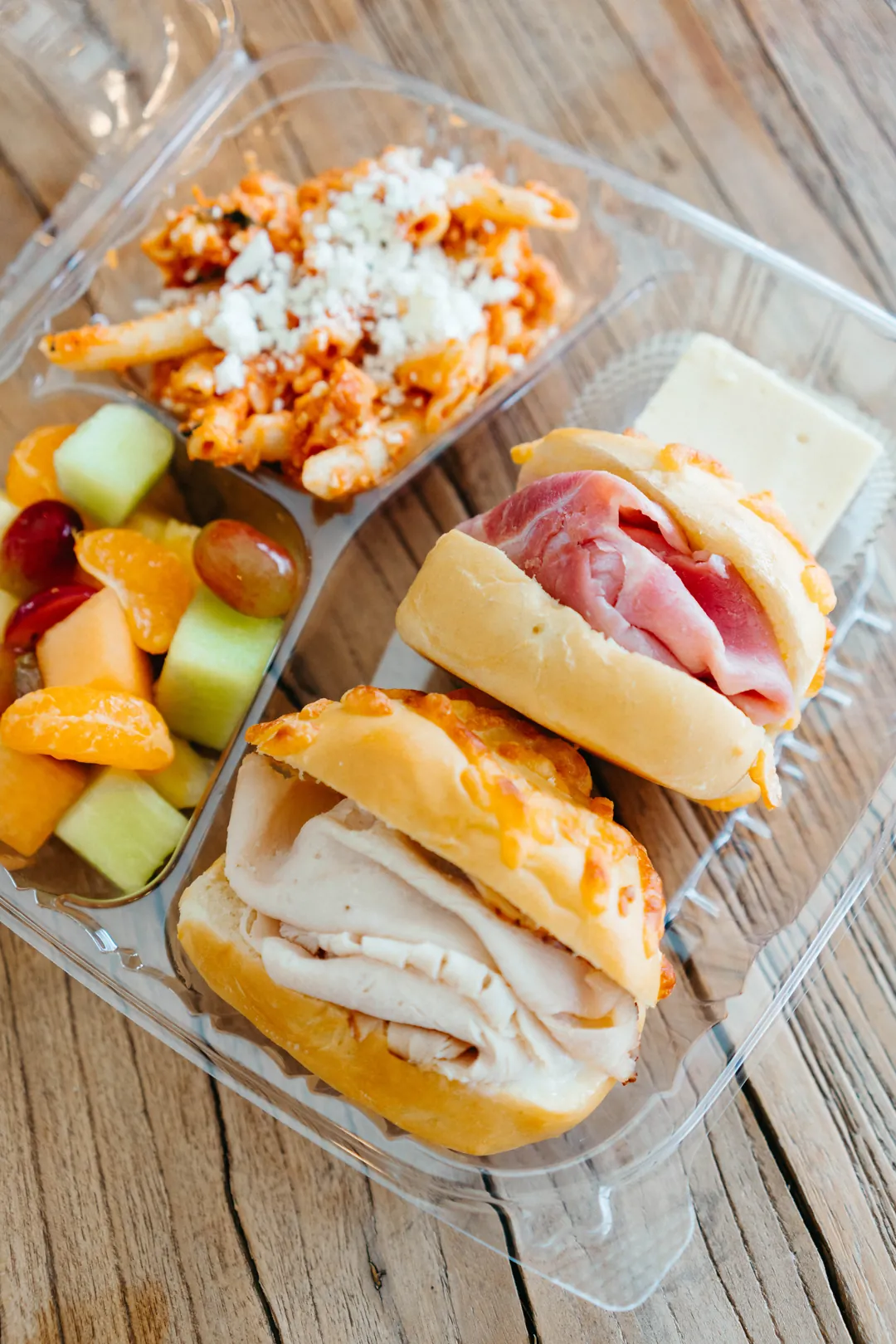 Boxed lunch with turkey and ham sandwiches, penne pasta, fruit, cheese and crackers