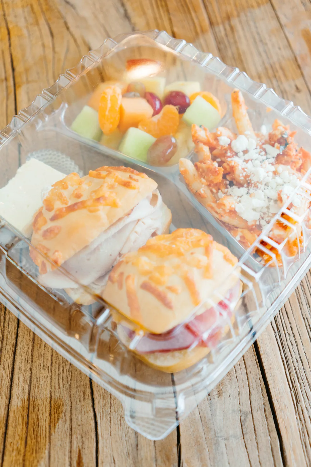 Open boxed lunch with turkey and ham sandwiches, penne pasta, fruit, cheese and crackers