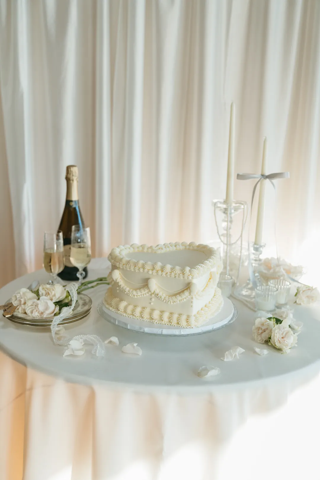 Ivory heart-shaped cake and champagne on a white table