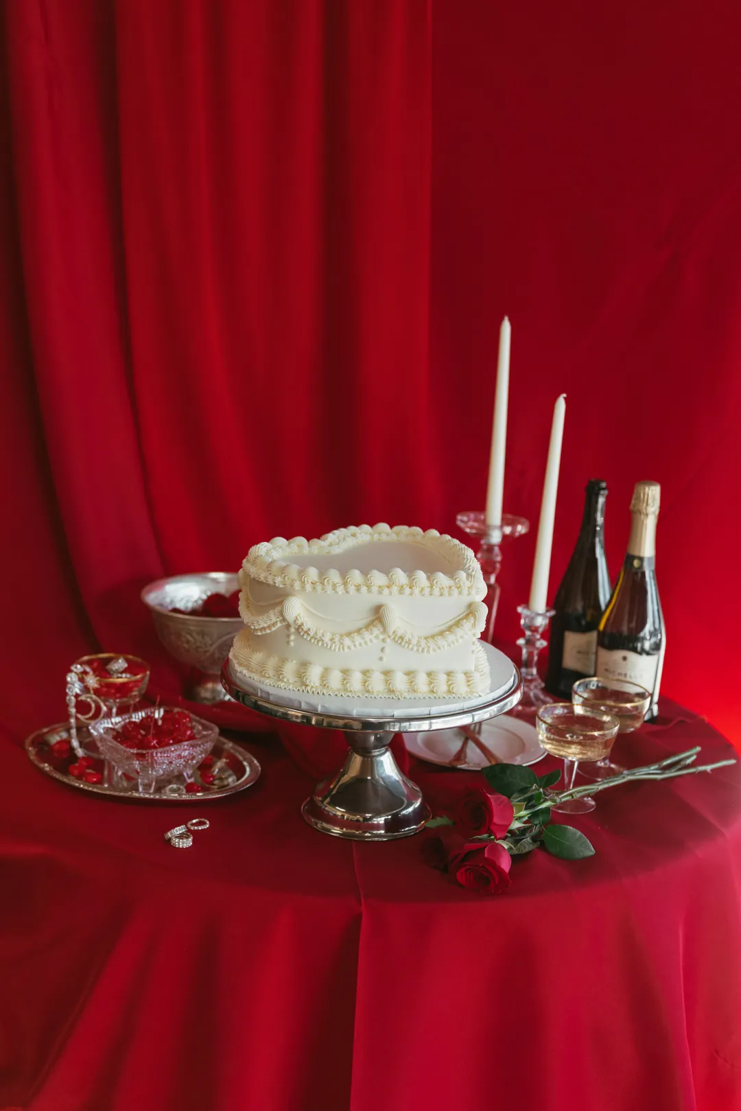 Heart-shaped cake, champagne, and candles on a red Valentine table