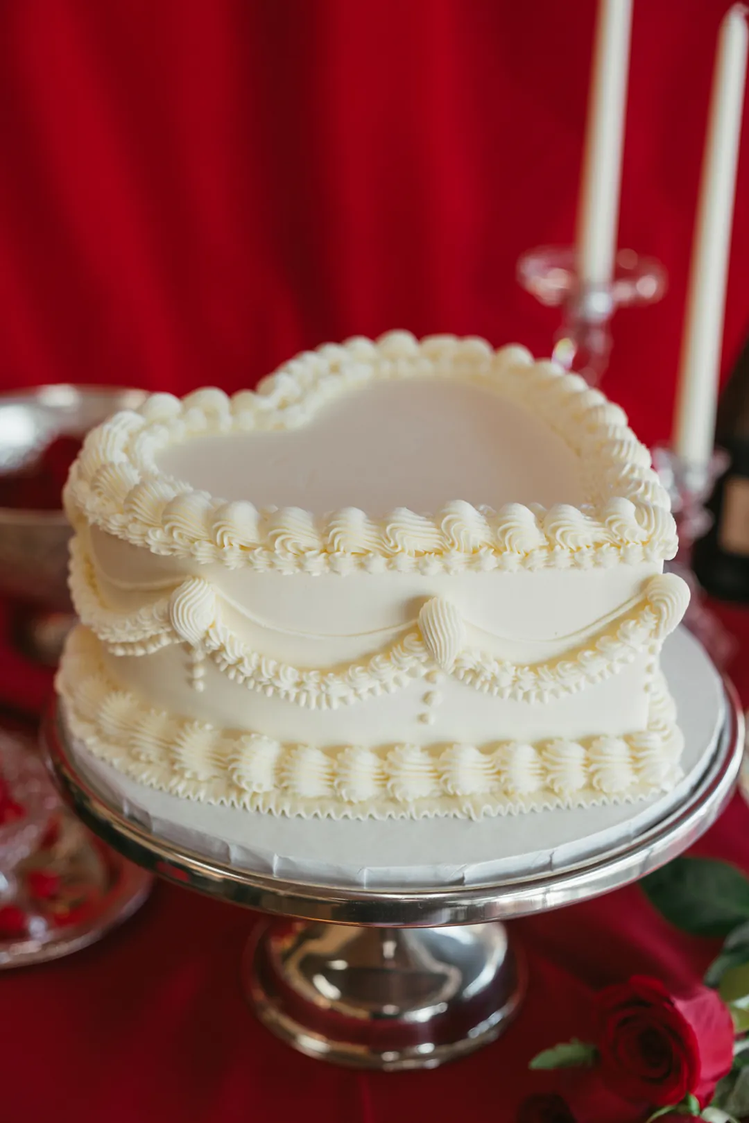 Ivory heart-shaped cake on a silver stand against a red backdrop
