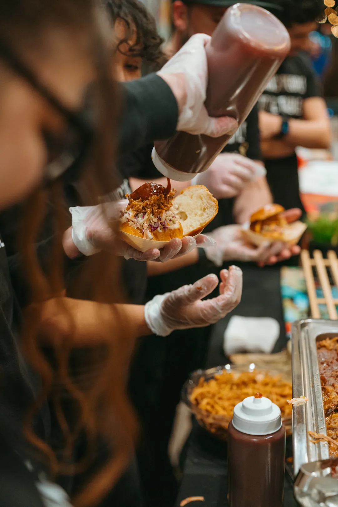 Kalua pulled pork sliders being dressed with barbecue sauce