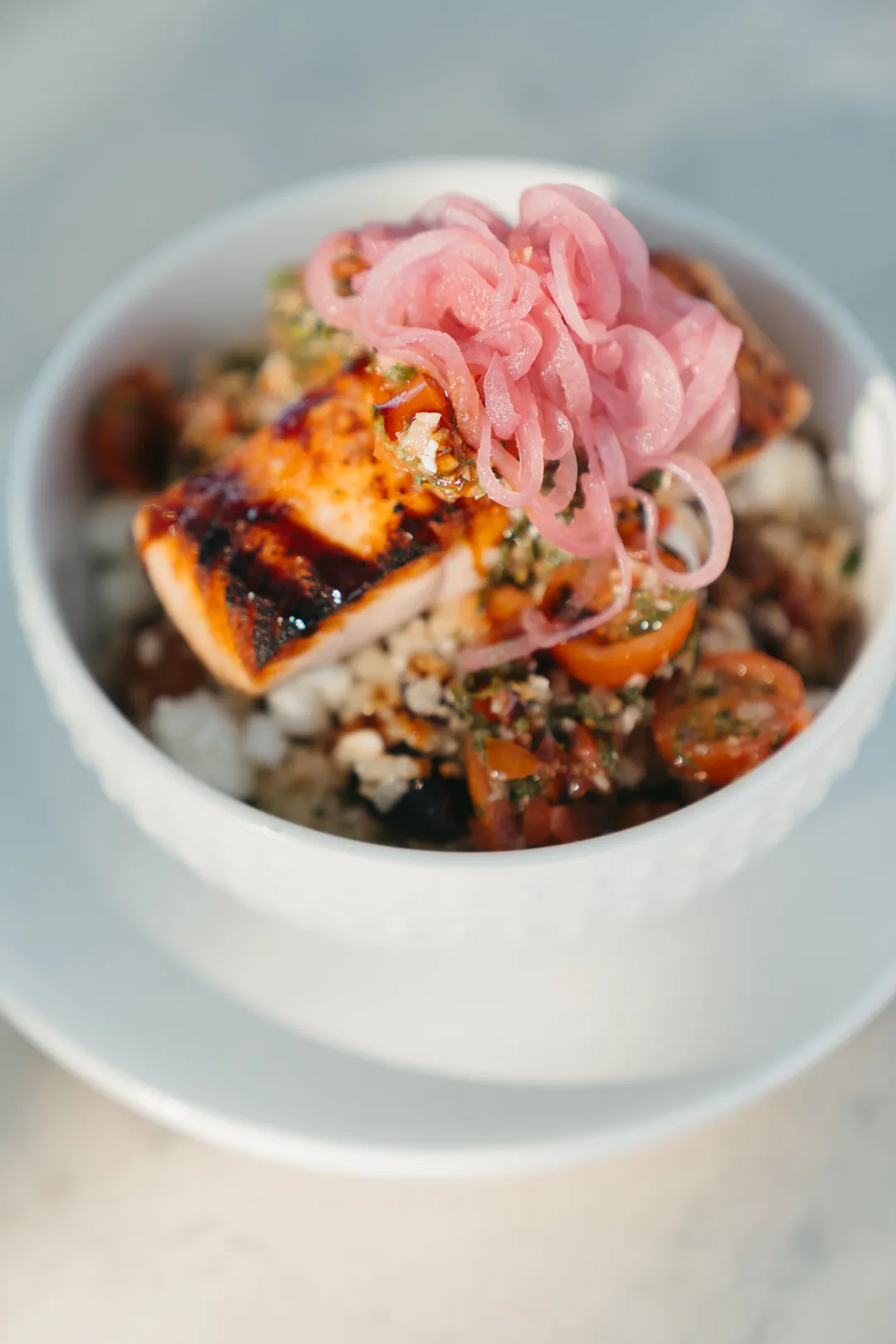 Greek quinoa salmon bowl topped with pickled onions