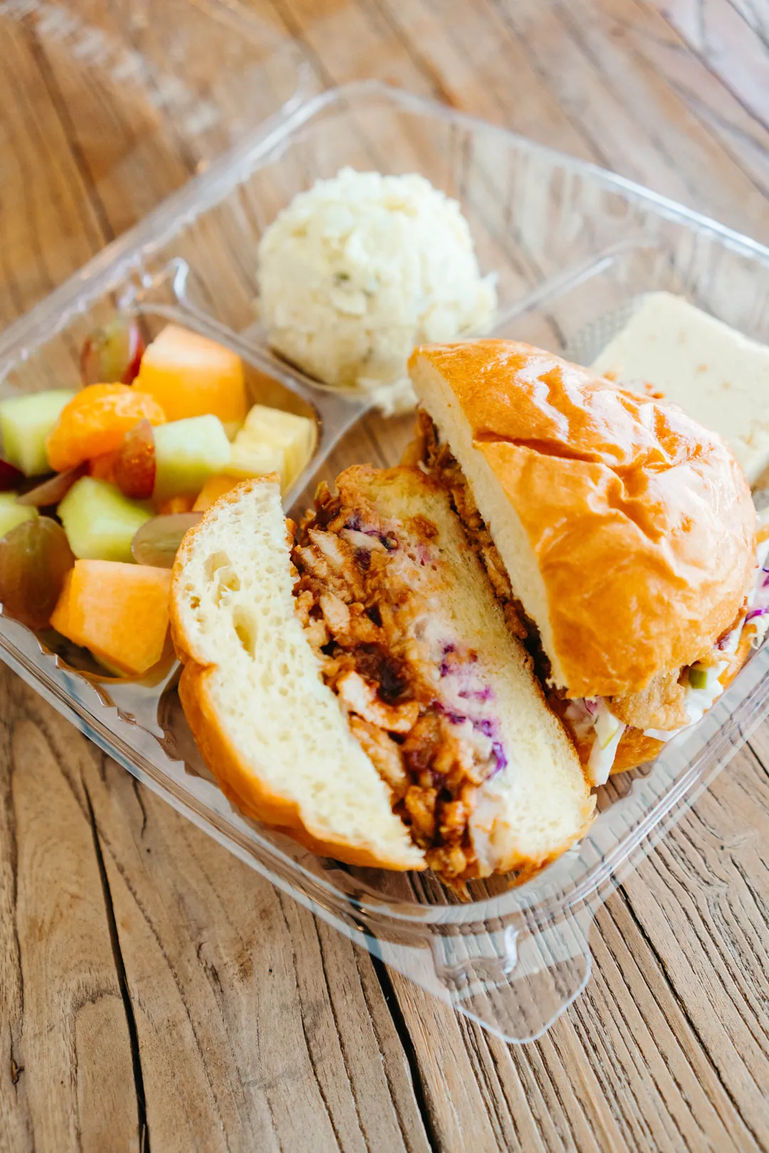 Boxed meal with a barbecue chicken sandwich, fruit, potato salad and dessert