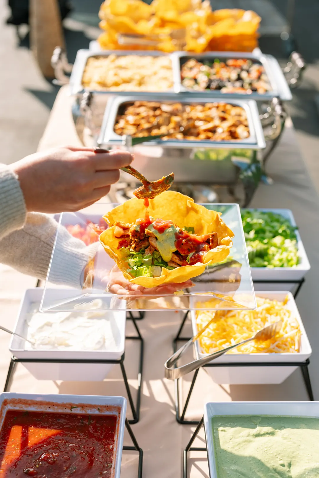 Guest spooning salsa onto a taco salad in a crisp tortilla bowl