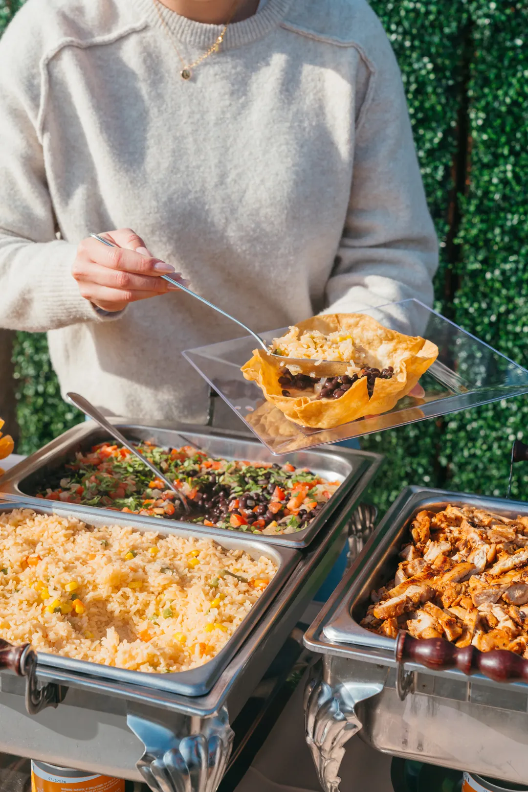 Guest adding rice to a tortilla bowl with beans beside grilled chicken