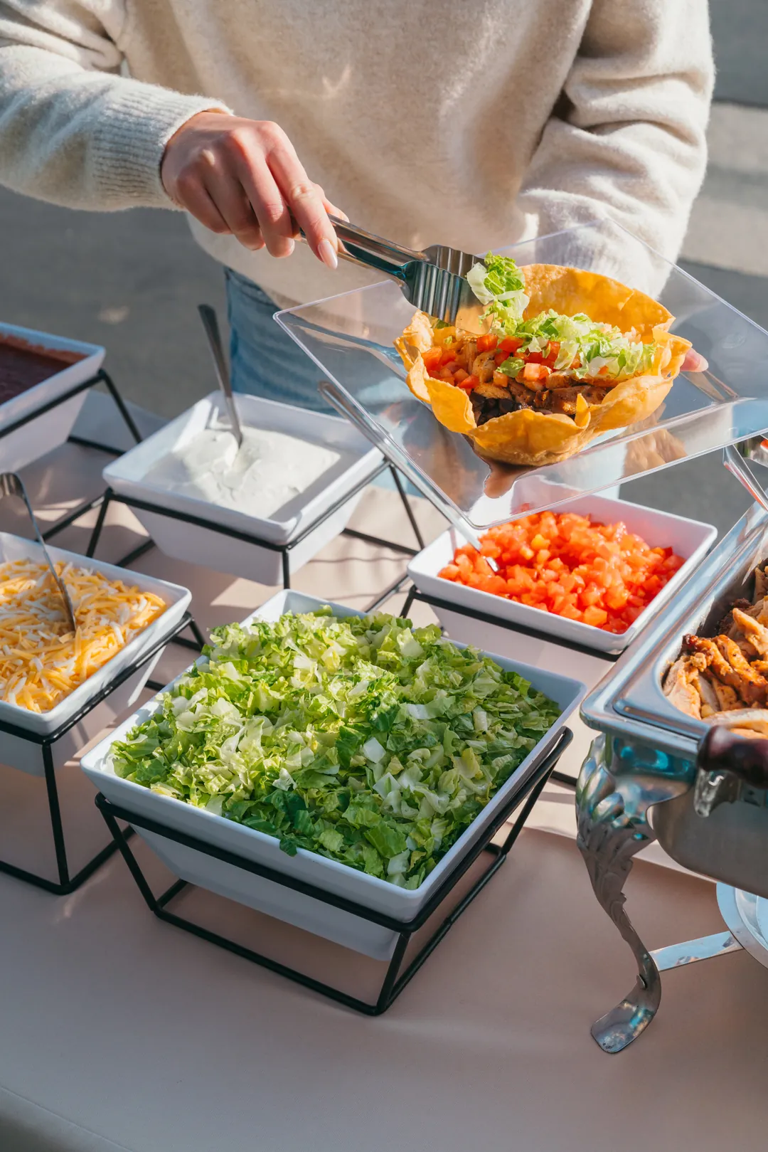 Guest adding lettuce to a taco salad in a crisp tortilla bowl