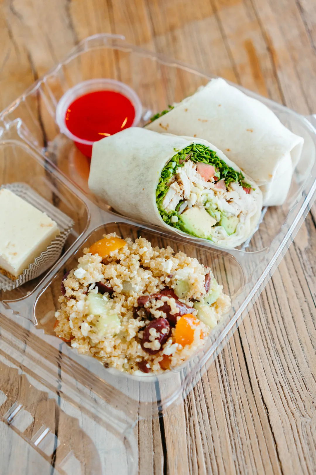 Boxed meal with a chicken avocado wrap, quinoa salad, dessert bar and red dressing