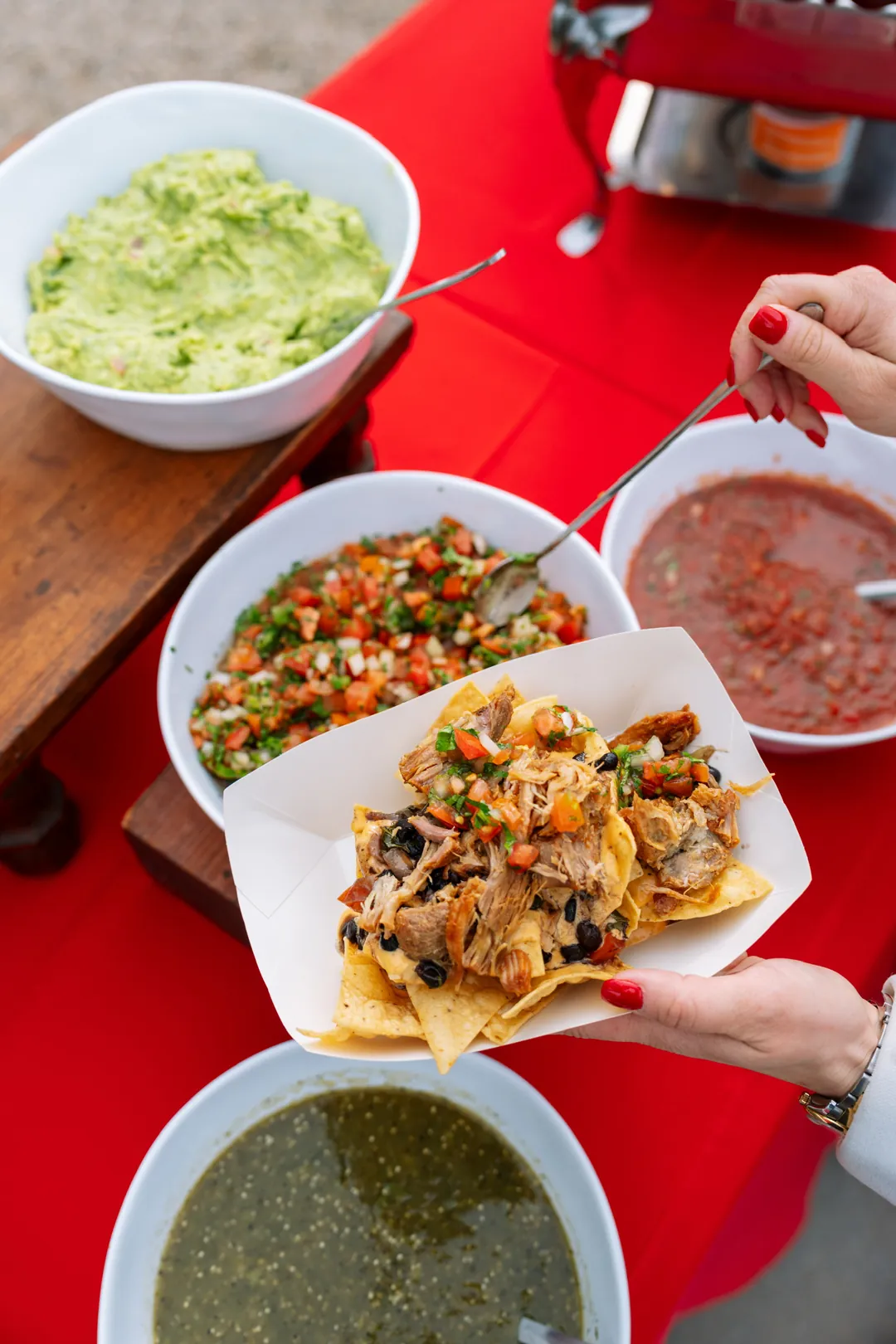Plate of loaded nachos beside bowls of salsa and guacamole