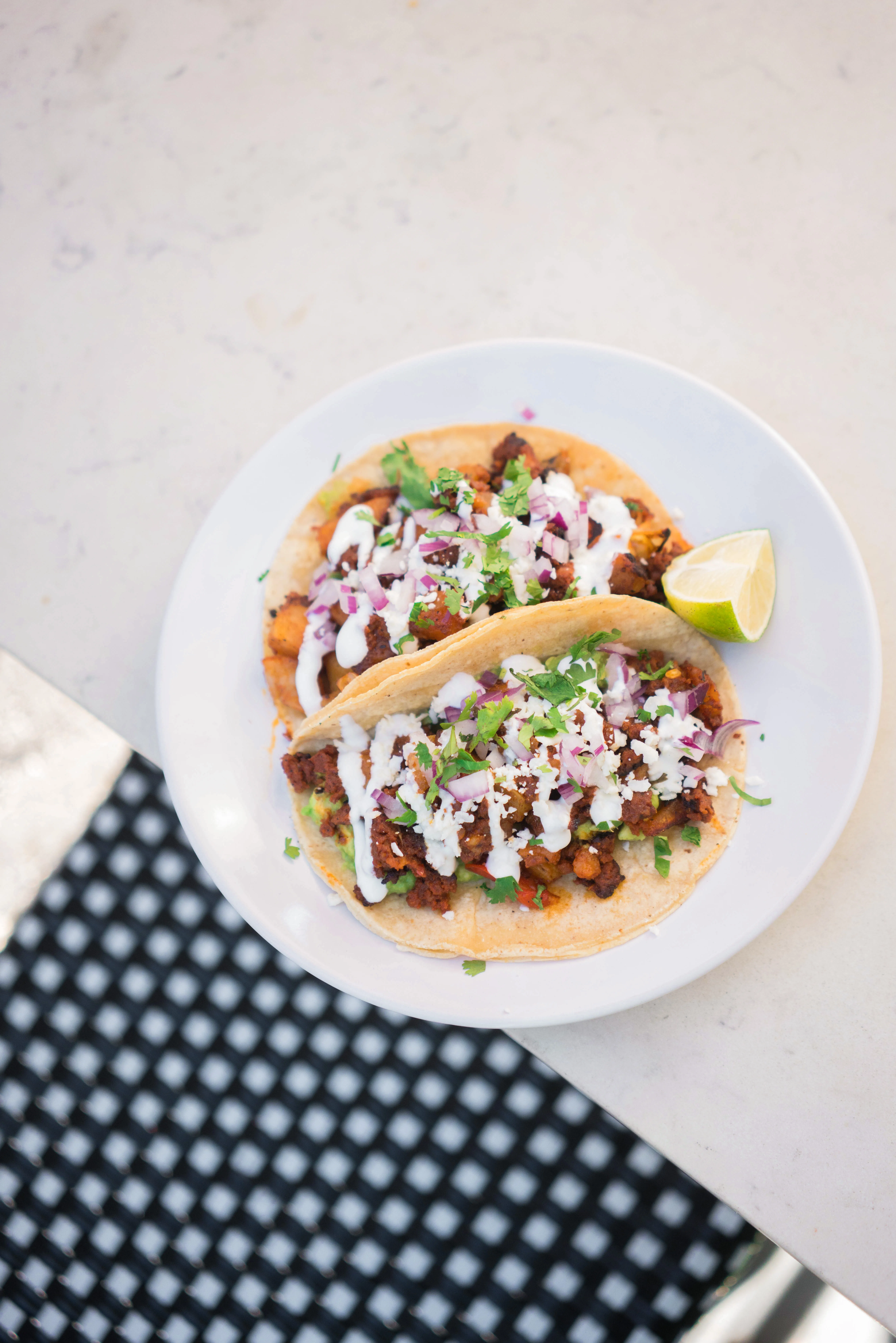 Two chorizo con papas tacos with crema, cheese, cilantro, and lime